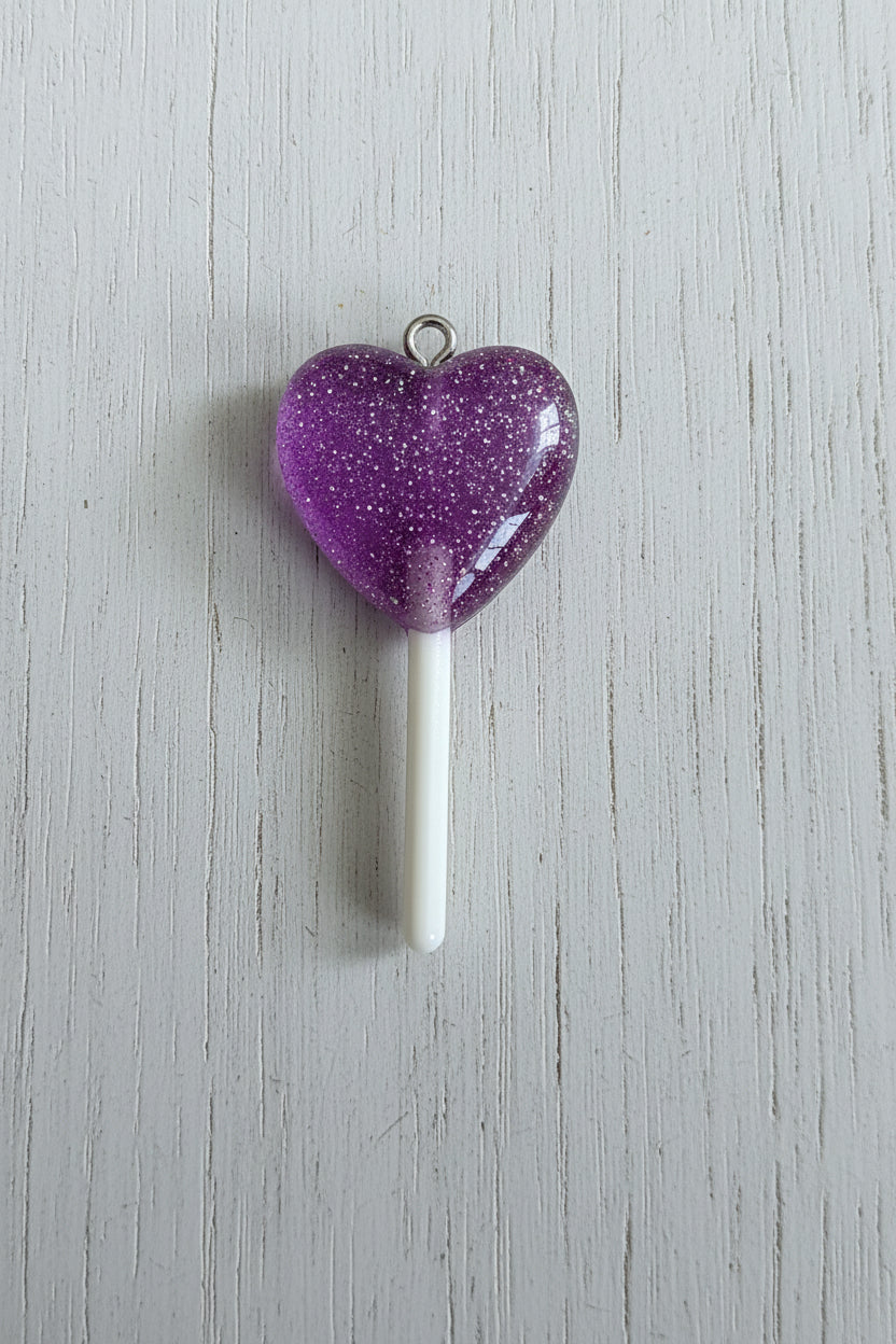 A translucent purple heart-shaped lollipop charm with a white stick and a small metal loop at the top.