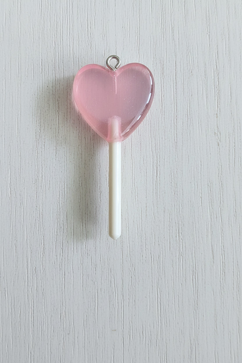 A heart-shaped translucent pink lollipop charm with a white stick and a small metal loop at the top.