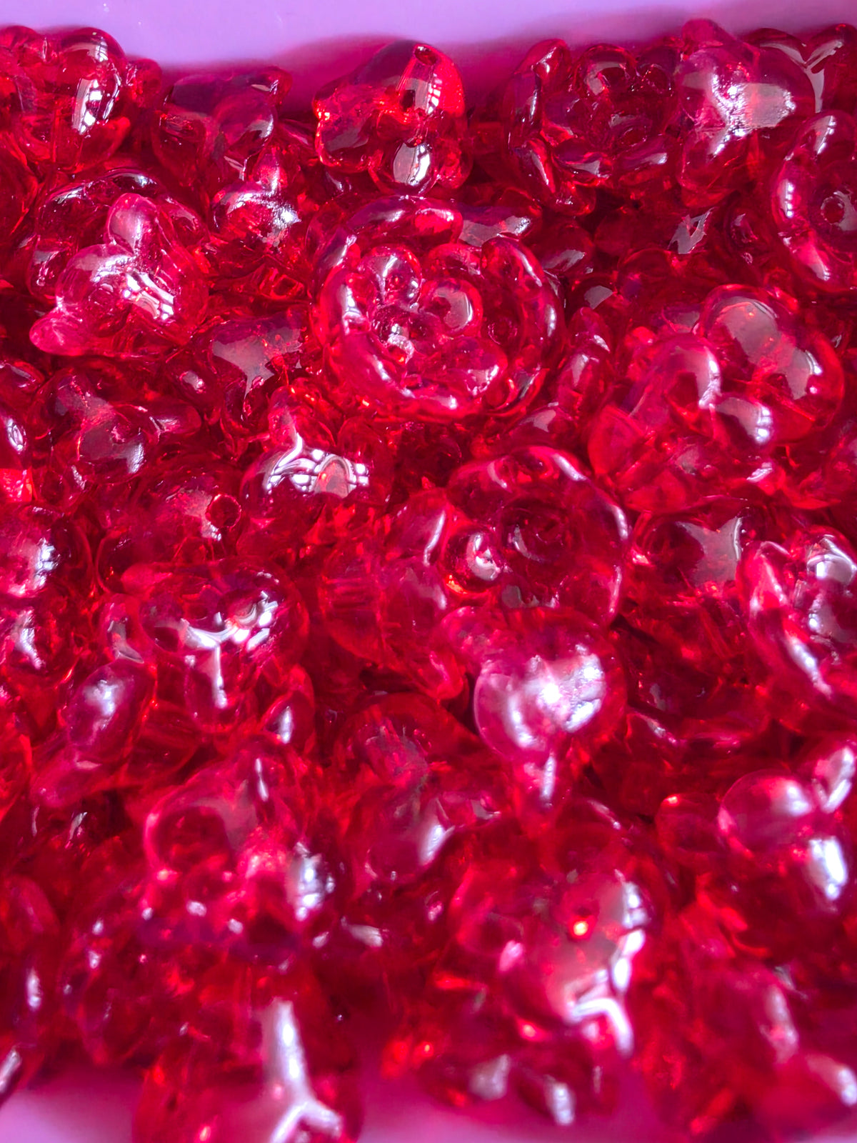 A close-up pile of translucent red glass flower-shaped beads.