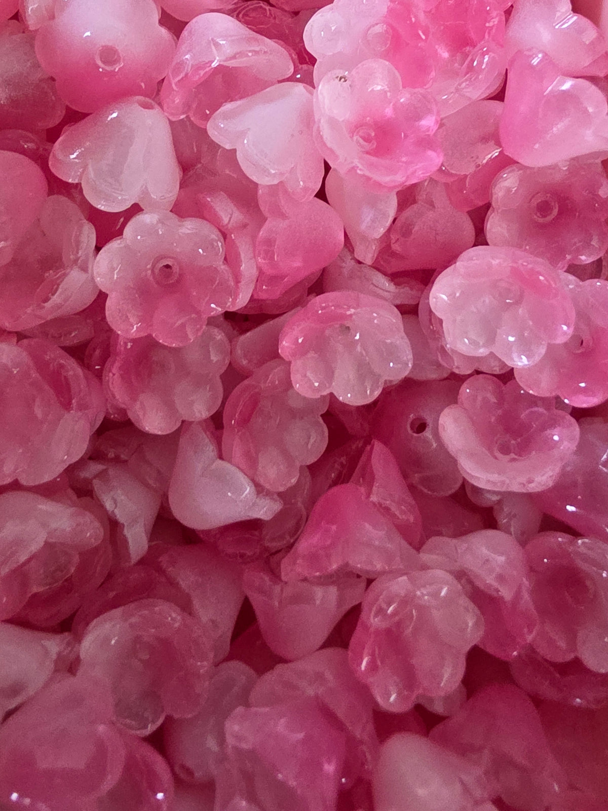 A close-up pile of glass pink flower-shaped beads with small holes.
