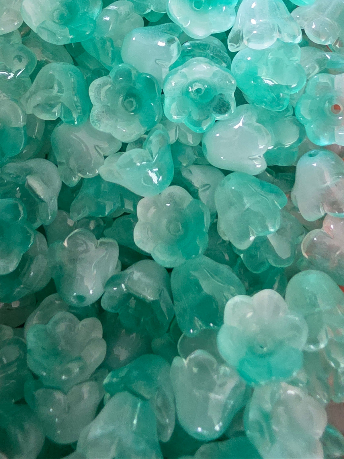 A close-up pile of small glass flower-shaped beads in aqua and turquoise tones.