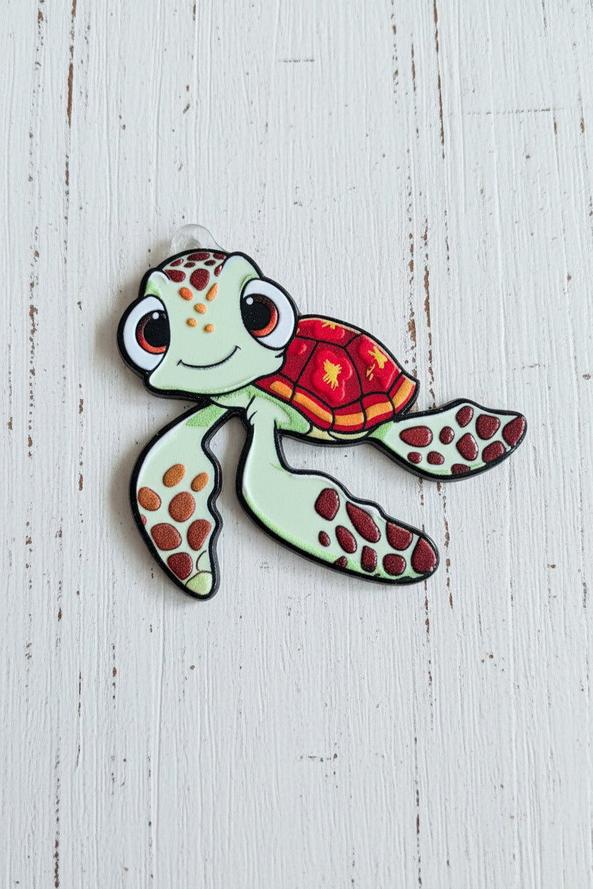 A cartoon sea turtle acrylic tag with a light green body, red and orange patterned shell and flippers, and large black eyes.