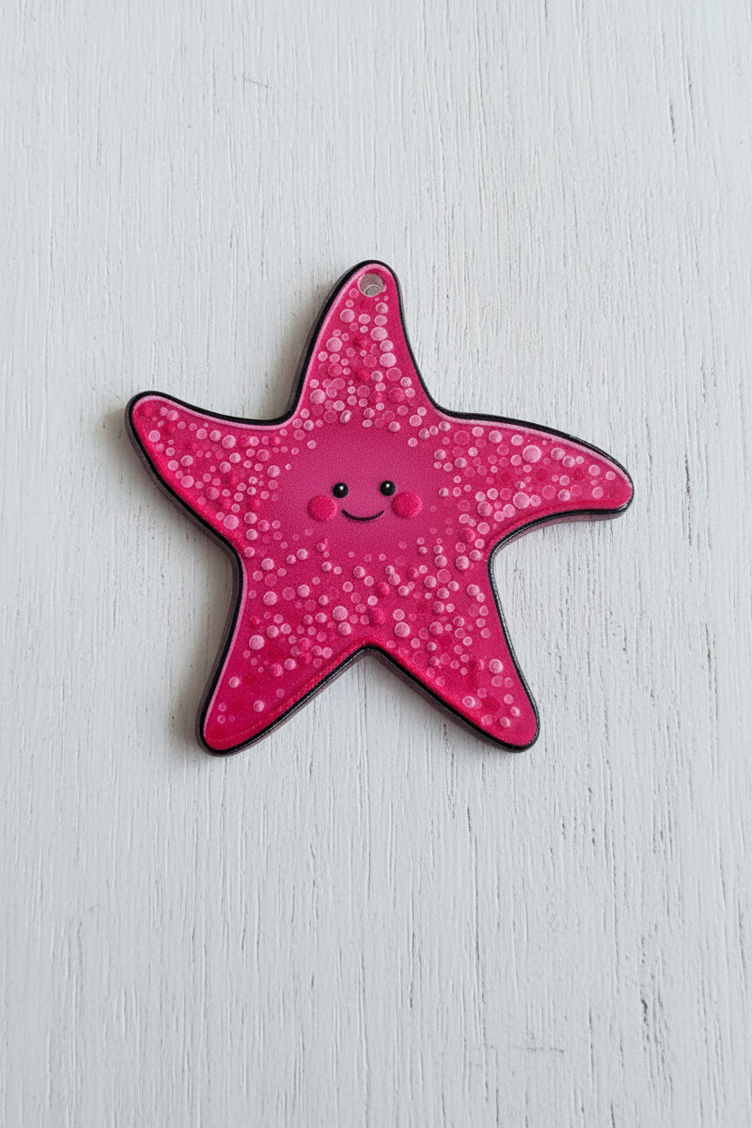 A pink starfish-shaped acrylic tag with a smiling face, covered in small white dots.