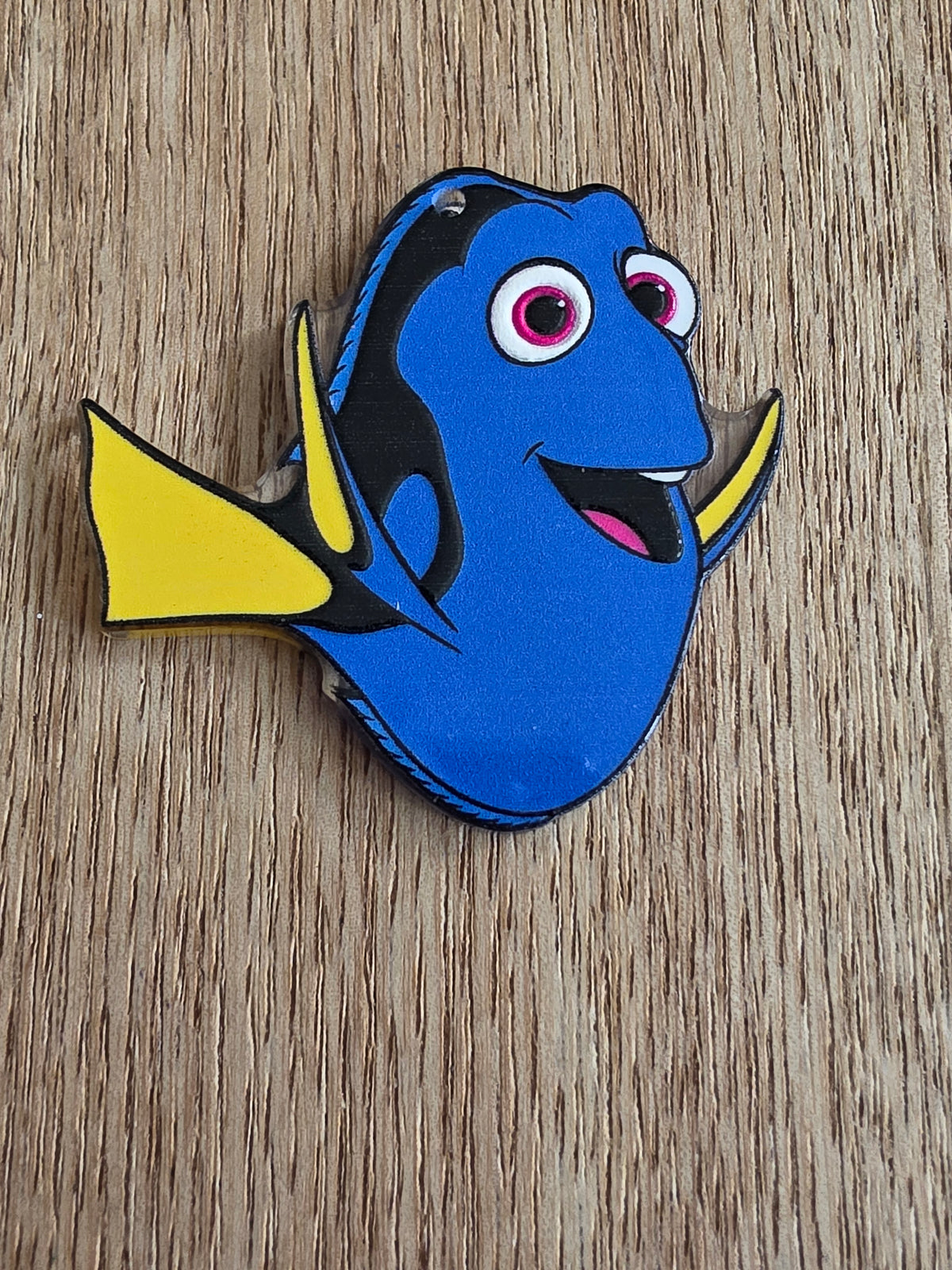 A cartoon fish-shaped acrylic bead with a blue body, yellow fins, and black details.