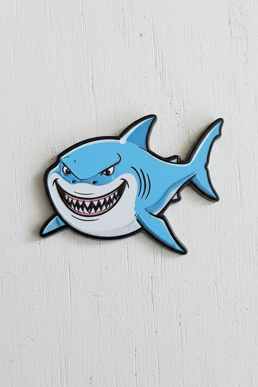 A cartoon shark acrylic bead with a wide grin and sharp teeth, colored in light blue and white with black outlines.