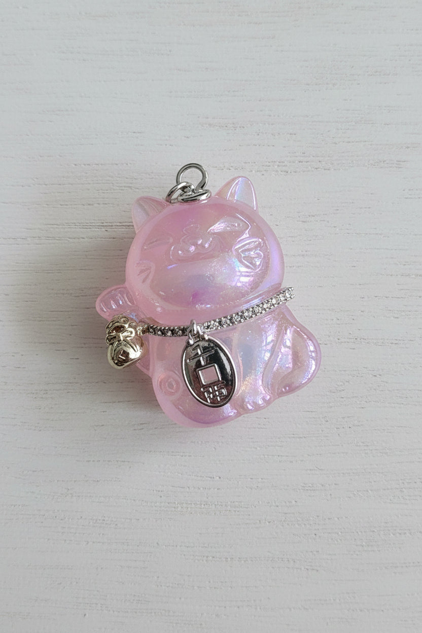 A pink iridescent cat-shaped pendant charm with gold-tone metal accents, including a chain, small bell, and oval tag.