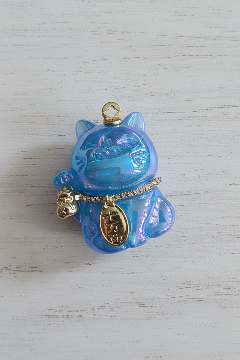 A blue iridescent lucky cat pendant with gold-tone details, including a bell, charm, and collar.