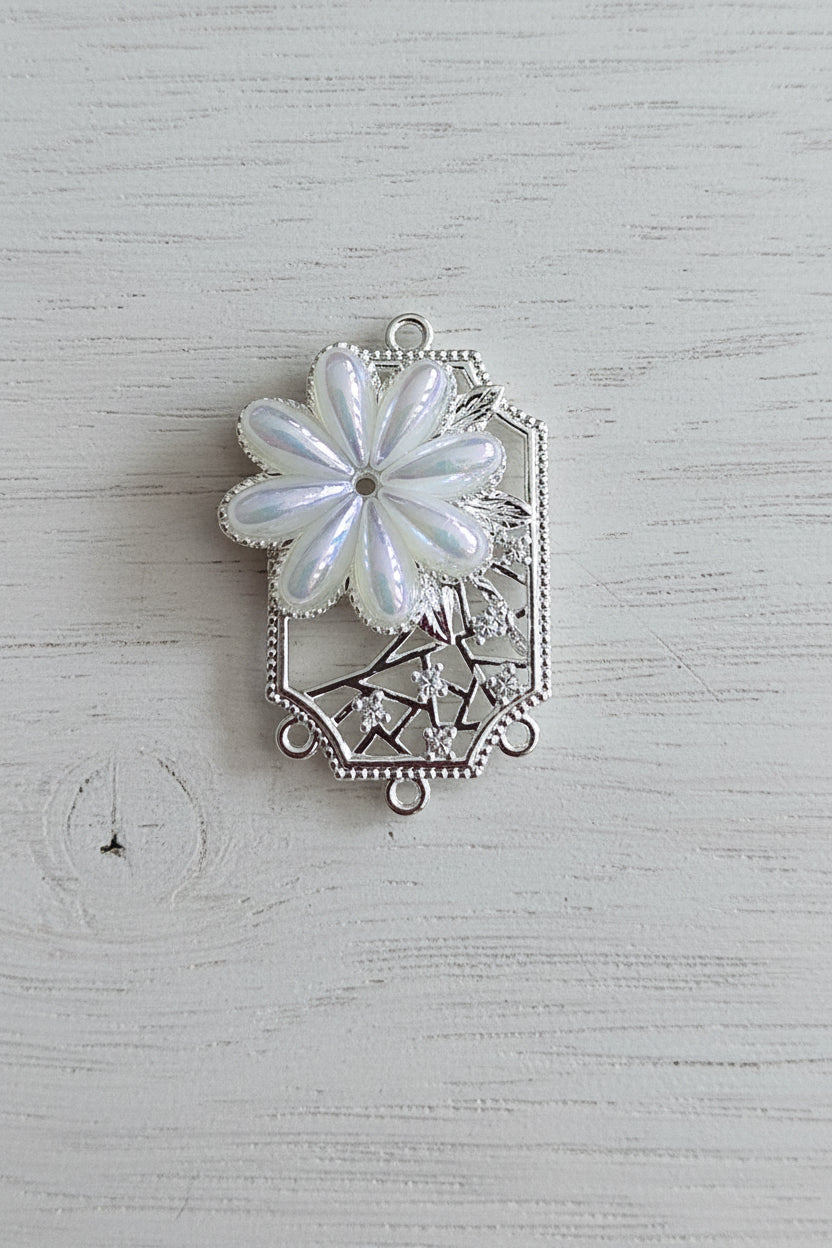 A silver-toned filigree jewellery connector featuring a large iridescent white flower.