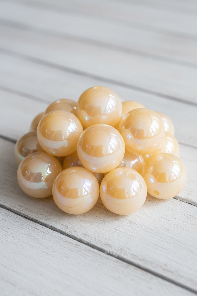 A close-up pile of glossy, iridescent peach-beige round beads with a small hole, reflecting light and showing a rainbow sheen.