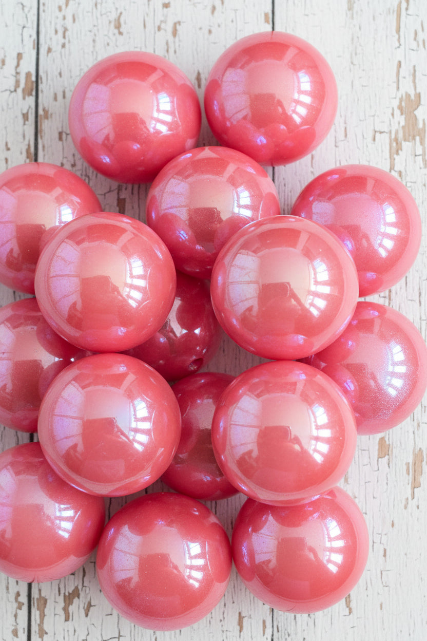 A close-up of multiple glossy, iridescent pink resin beads,  showing reflective highlights and a subtle sheen.