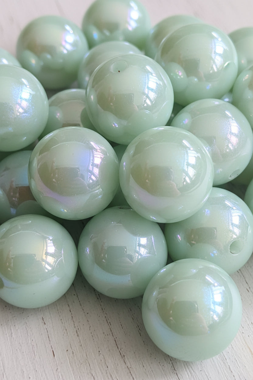 A close-up of glossy, iridescent resin beads in a pale blue color with a pearlescent finish. The beads are arranged closely together, filling the entire frame, with small holes visible on several beads.