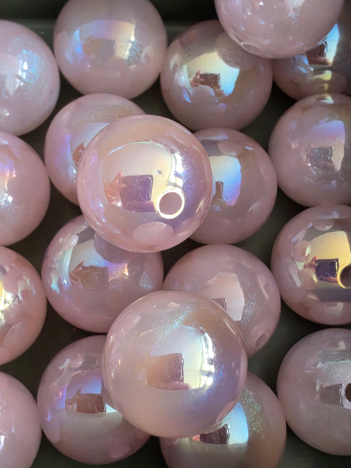 A close-up pile of round, iridescent purple beads with a pearlescent finish reflecting light.