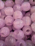 A close-up pile of round purple beads filled with fine silver glitter, showing a glossy finish and iridescent sparkle.