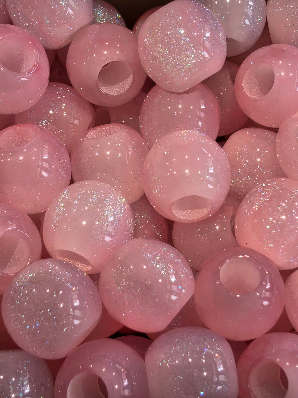 A close-up pile of round pink beads filled with fine silver glitter, showing glossy highlights and sparkling reflections.