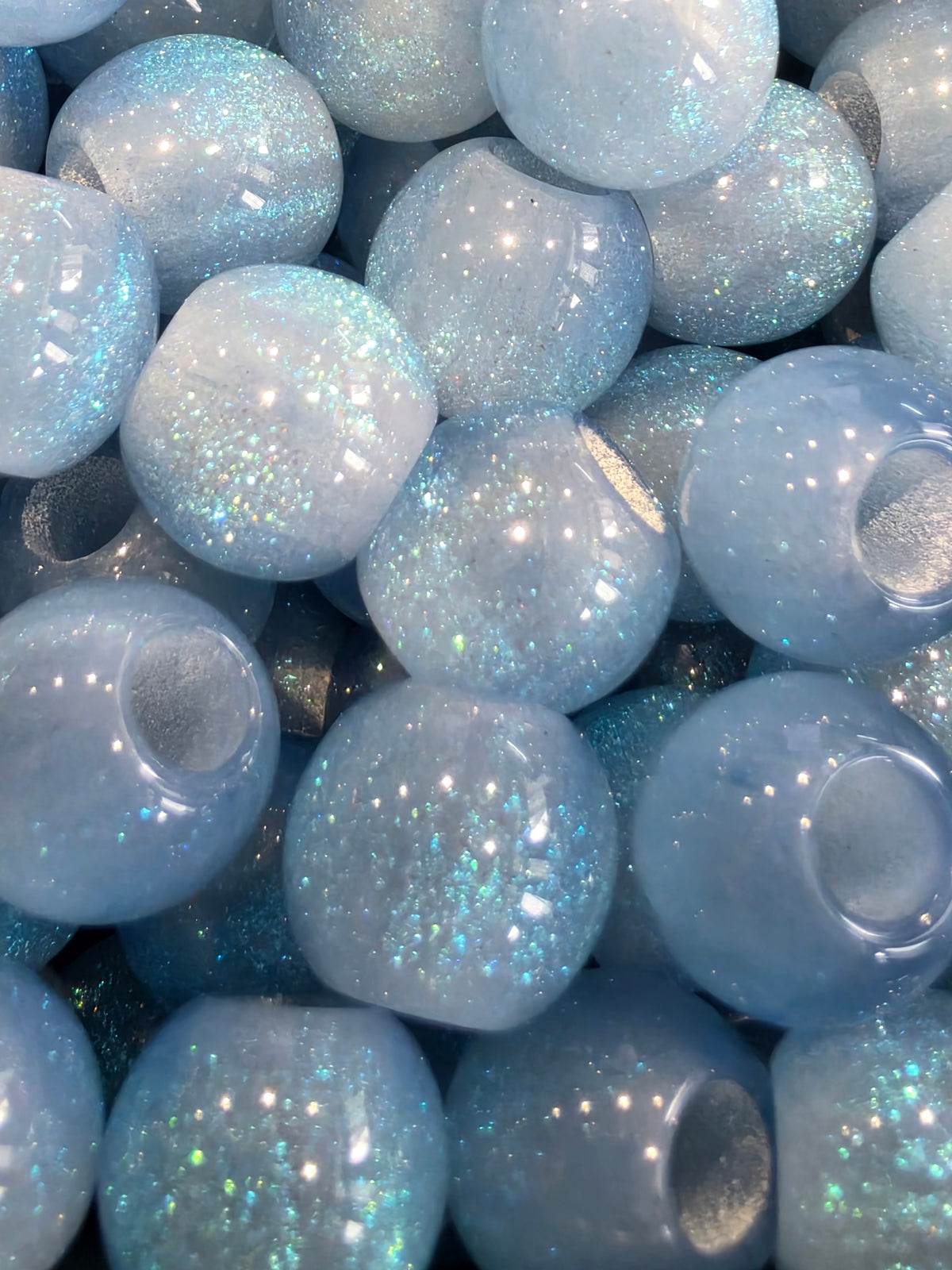 A close-up pile of round, glossy resin beads with a light blue iridescent glitter finish.