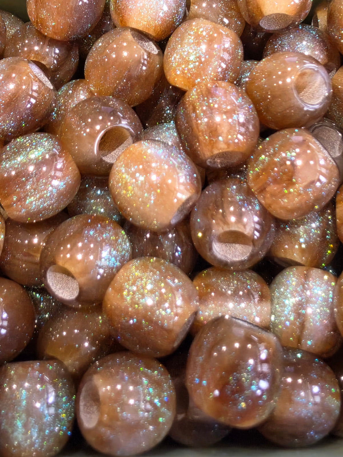A close-up pile of round, glossy brown  resin beads filled with iridescent glitter.