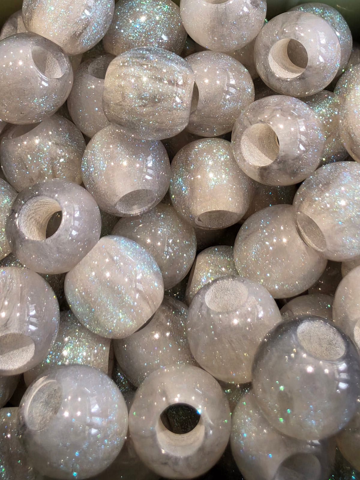 A close-up pile of  grey resin beads filled with iridescent silver glitter, showing a pearlescent sheen.