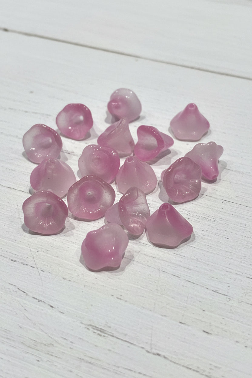 A close-up of several small, translucent pink flower-shaped glass beads.