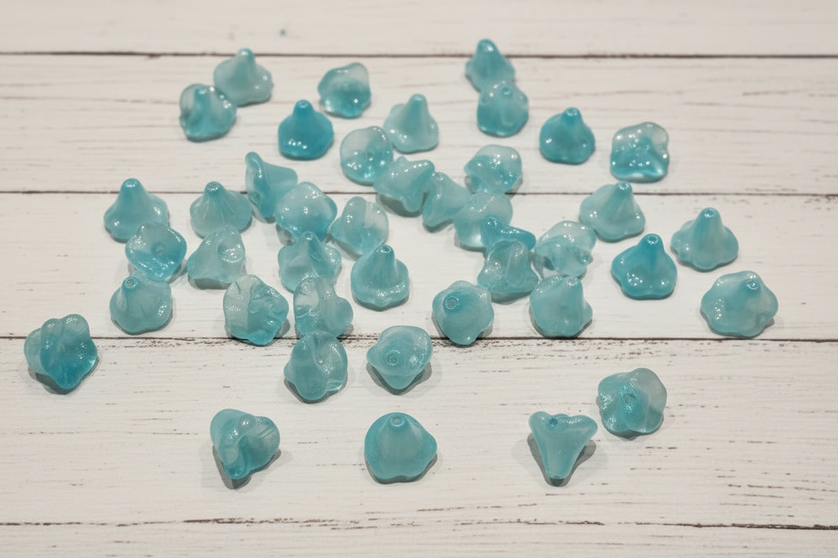 A hand holding several small translucent blue and white glass flower beads.