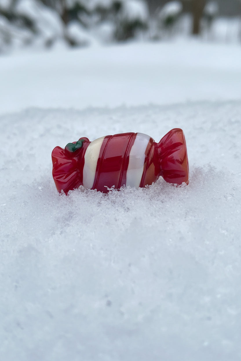 A glossy red and white striped candy-shaped bead with a small green accent.