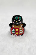 A glossy black gingerbread bead decorated with a green bow, brown scarf, red coat, and white details.