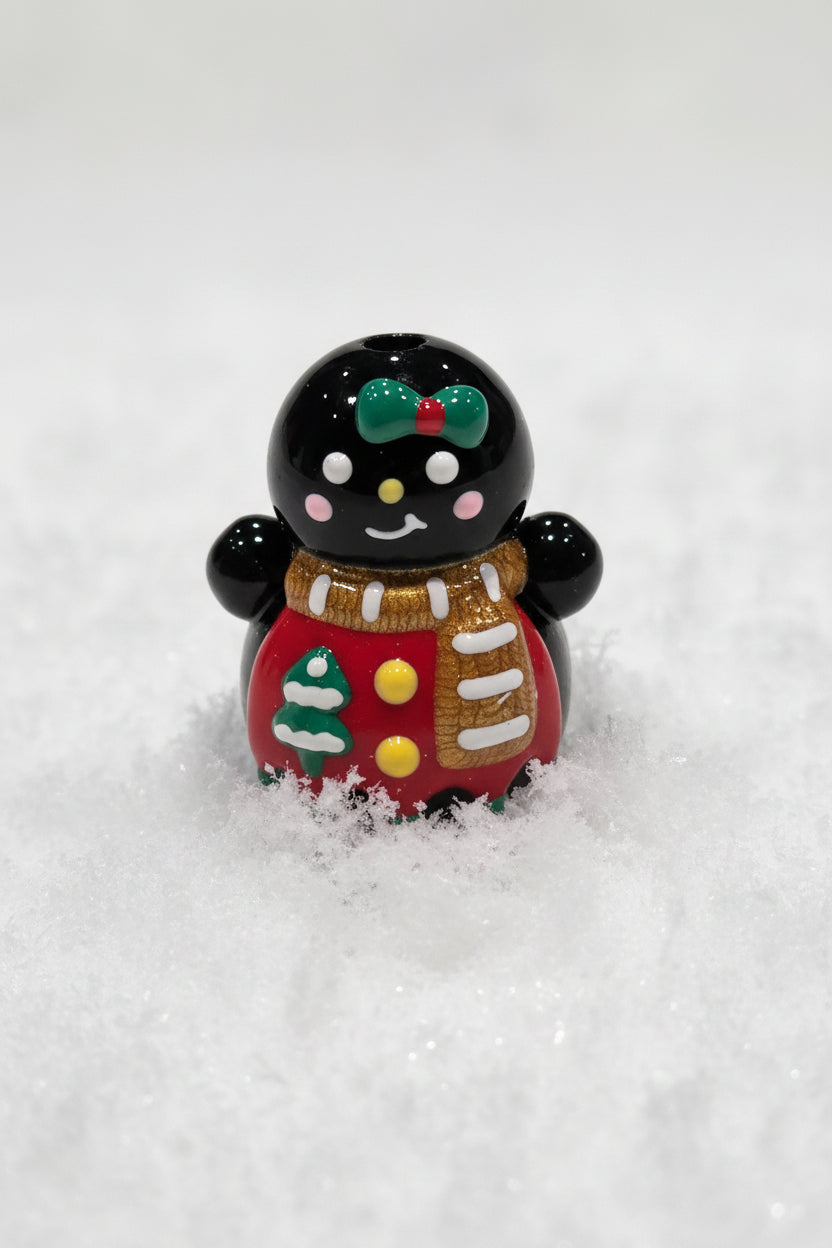 A glossy black gingerbread bead decorated with a green bow, brown scarf, red coat, and white details.