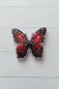 A butterfly-shaped acrylic bead with glittery red and black wings, featuring a rose pattern.