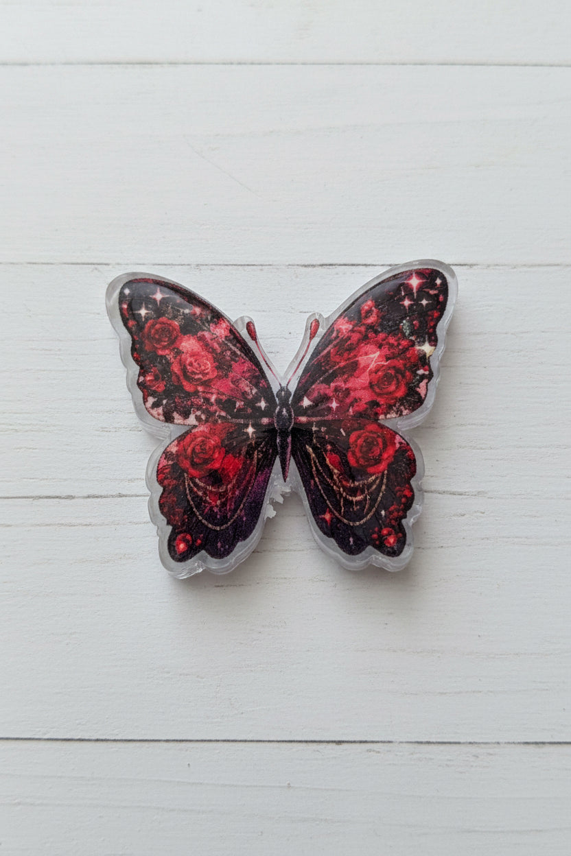 A butterfly-shaped acrylic bead with glittery red and black wings, featuring a rose pattern.