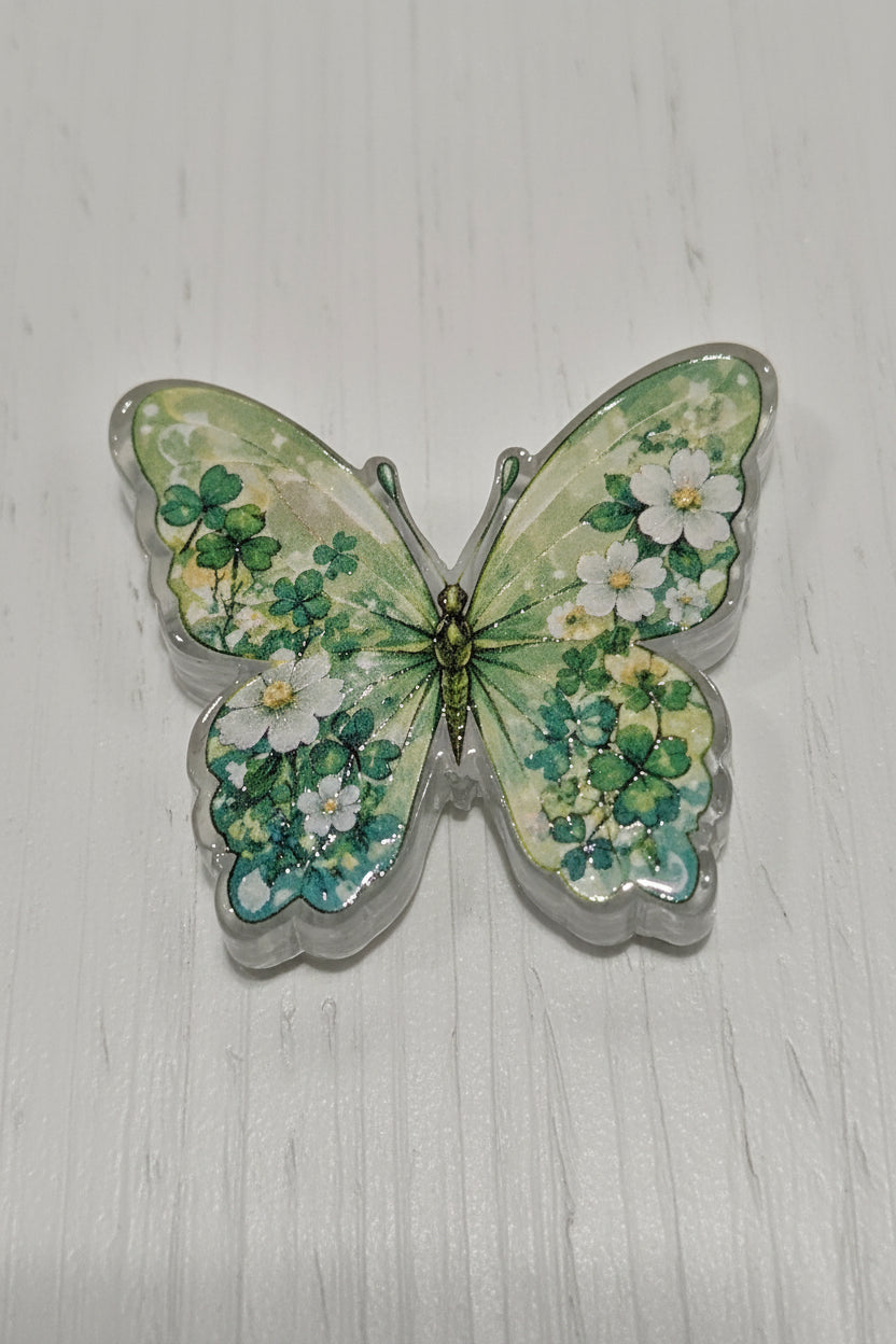 A butterfly-shaped acrylic bead with green clover and white flowers.