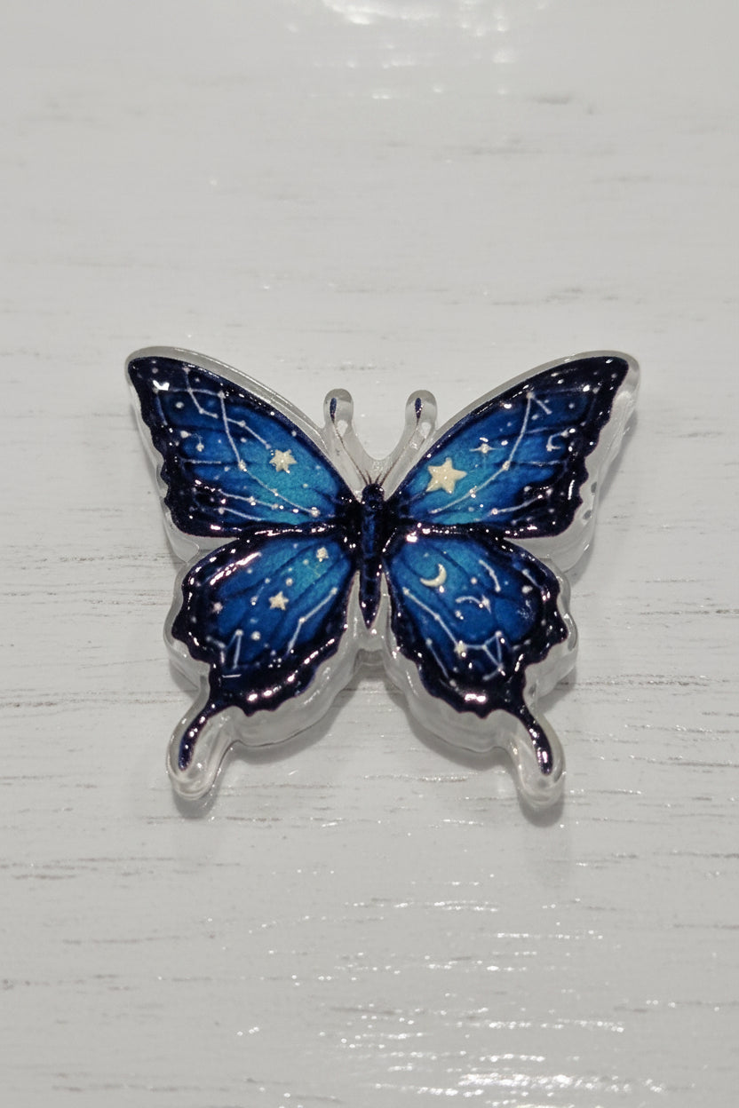 A butterfly-shaped acrylic bead with vibrant blue and black wings decorated with white star and moon details.