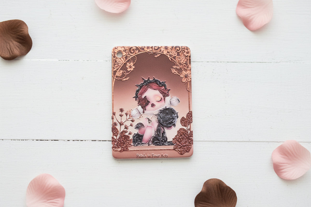 An acrylic tag with a rose-gold/copper-toned border and embossed floral details, featuring an illustration of a child with a crown and a black cat.