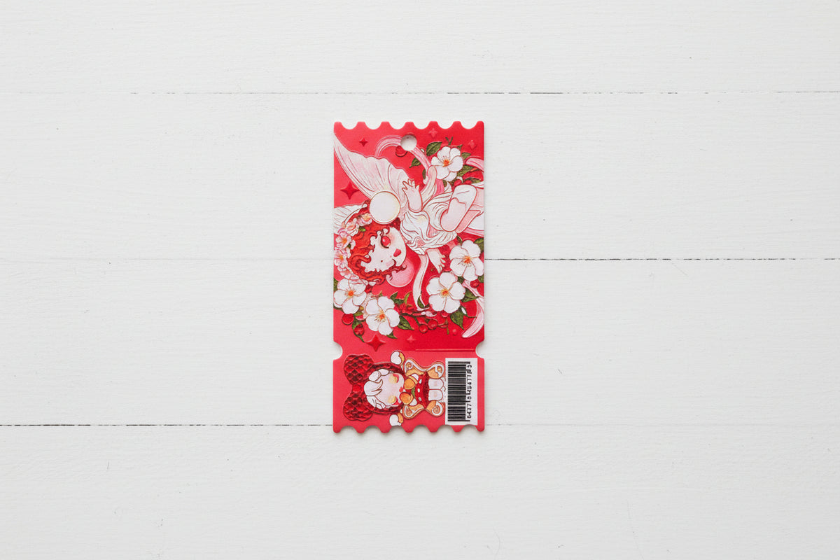A red tag with a scalloped bottom edge, featuring anime-style artwork of a white-haired character, cherub wings, cherry blossoms, and a small cartoon figure near the bottom. A barcode sticker is attached on the lower right.