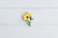 A small enamel charm shaped like a yellow sunflower with a bee on the stem.