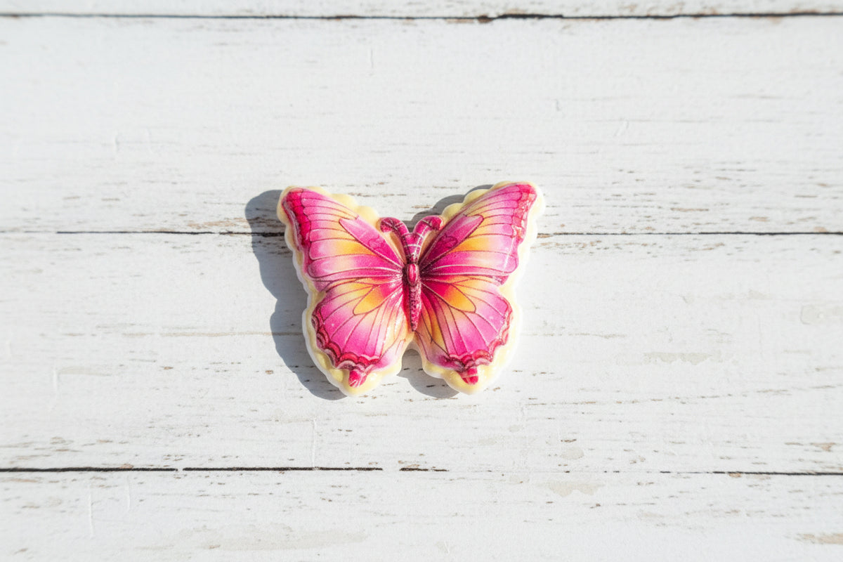 A butterfly-shaped acrylic bead with pink and yellow gradient wings outlined in white.