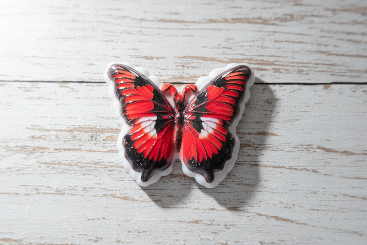 A butterfly-shaped acrylic bead with vibrant red, black, and white wings.