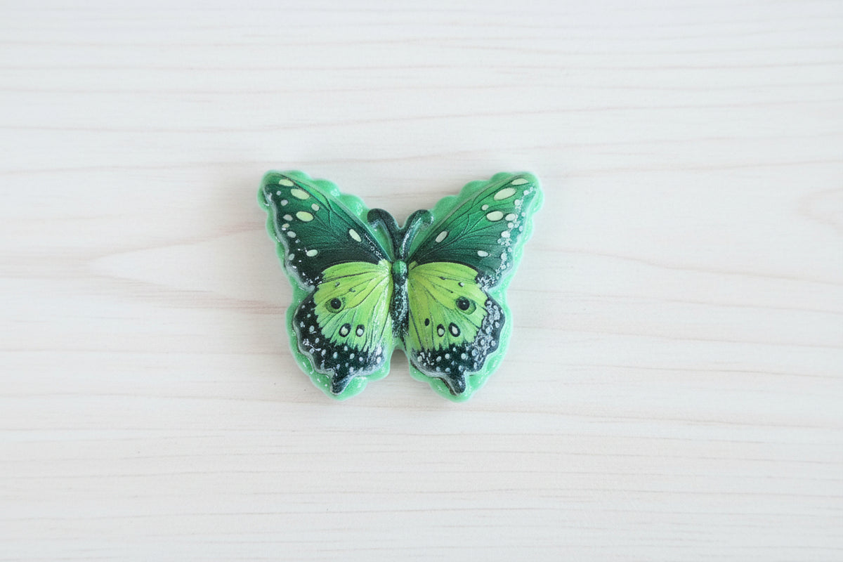 A green butterfly-shaped acrylic bead with black and white spotted wing patterns.