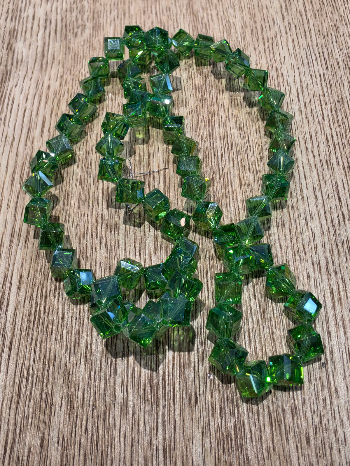 A strand of  green glass beads arranged in a loose loop on a light brown wood-grain surface.