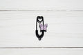 A black safety pin-shaped charm with a small lavender butterfly and heart design, placed on a light wood grain surface.