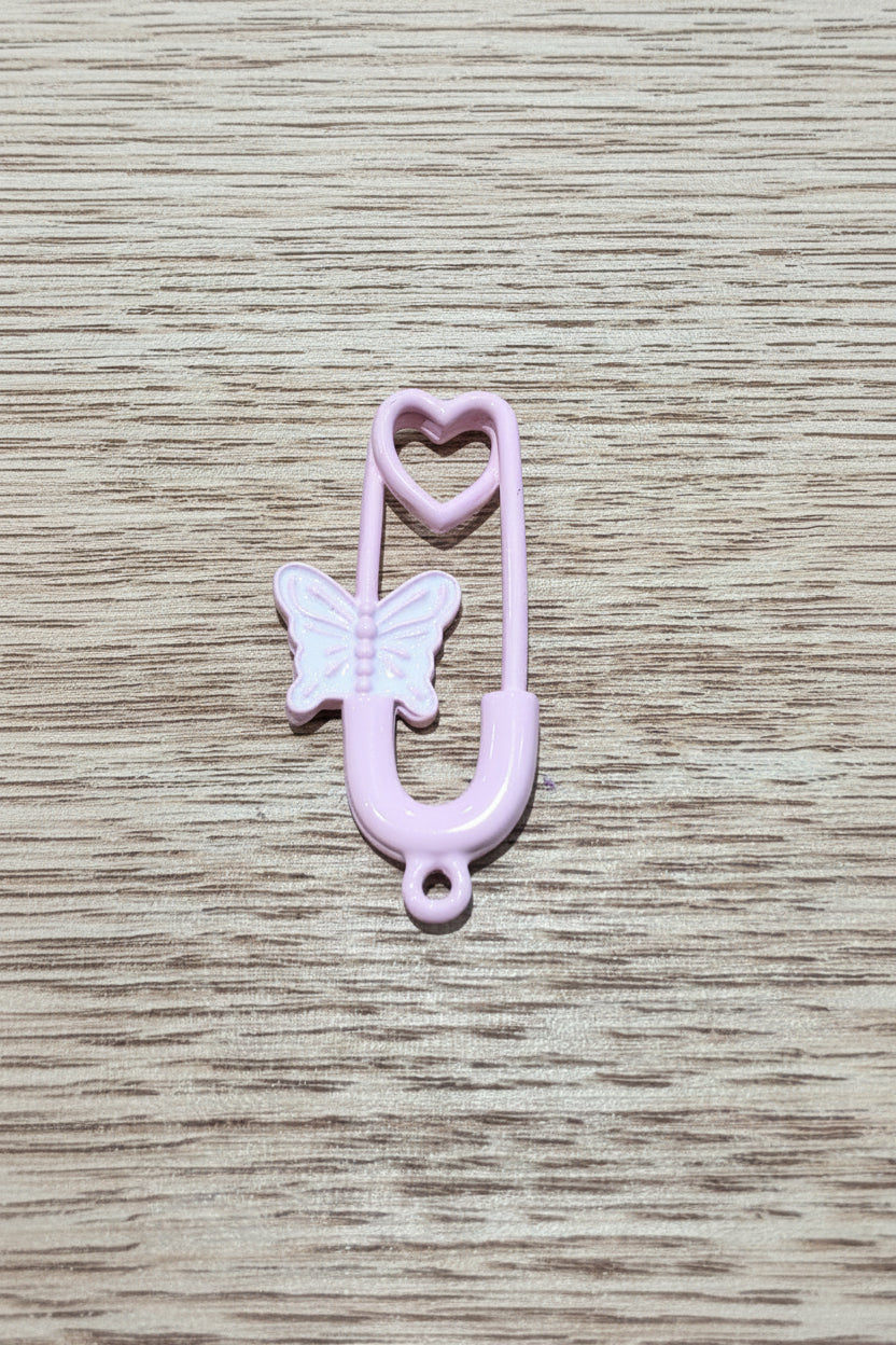 A light pink safety pendant with a butterfly and heart details, resting on a light brown wood-grain surface