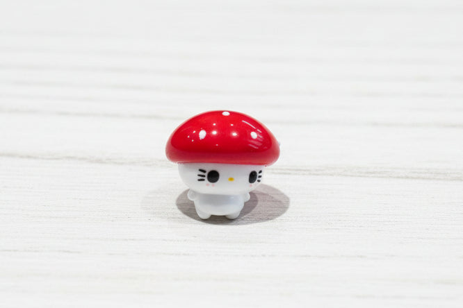A small mushroom-shaped bead with a red cap and white body, resting on a textured wooden surface.