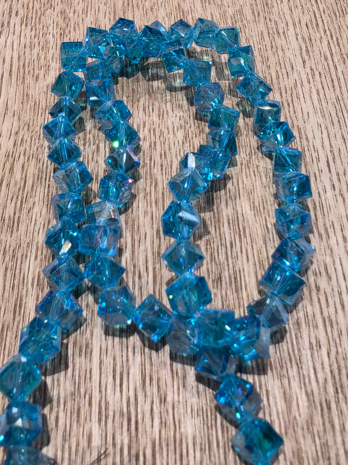 Blue glass crystal beads arranged in loops on a light brown wood grain surface.