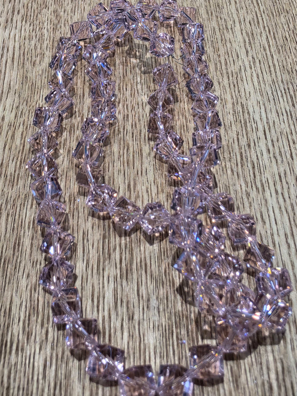 A strand of pink glass beads, arranged in a loop on a light brown wood grain surface.