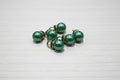 Green pearl-like pendant with gold-toned metal caps and loops, displayed on a light brown wood-grain surface.