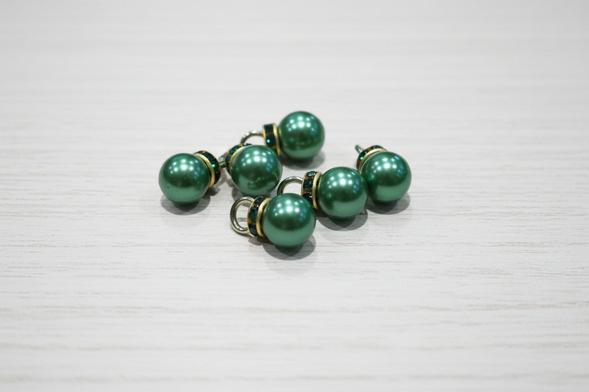 Green pearl-like pendant with gold-toned metal caps and loops, displayed on a light brown wood-grain surface.