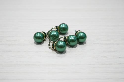 Green pearl-like pendant with gold-toned metal caps and loops, displayed on a light brown wood-grain surface.