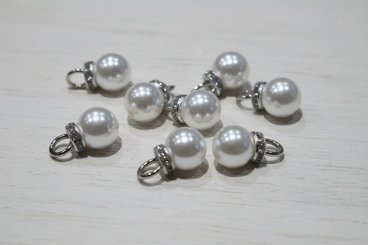 white pear-like pendant beads with silver-toned metal loops and textured spacer bands, scattered on a light brown wood grain surface.