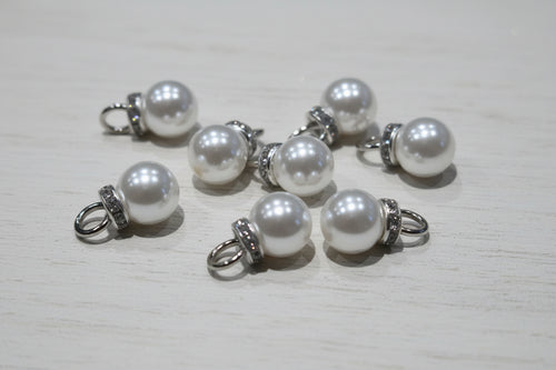 white pear-like pendant beads with silver-toned metal loops and textured spacer bands, scattered on a light brown wood grain surface.