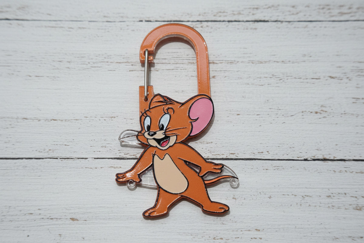 A mouse character keyring with a silver carabiner clip, resting on a light brown wood grain surface.