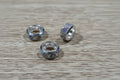 Three silver-toned spacer bead with multicolor iridescent glitter, arranged on a light brown wood grain surface.