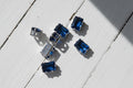 Rectangular blue zircon beads with silver-toned metal settings, scattered on a light brown wood grain surface